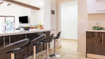 A modern kitchen with a bar area, bar stools, a TV, and a bowl of fruit.