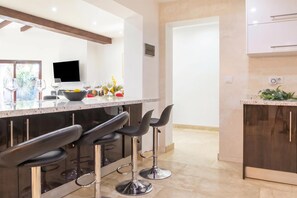 Una cucina moderna con angolo bar, sgabelli da bar, una TV e una ciotola di frutta.
