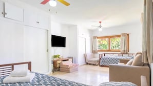 A bedroom with two beds, a desk, a chair, a TV, and a window with curtains.