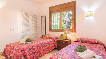 A bedroom with two beds, a window with a view, a nightstand, and a wall-mounted lamp.