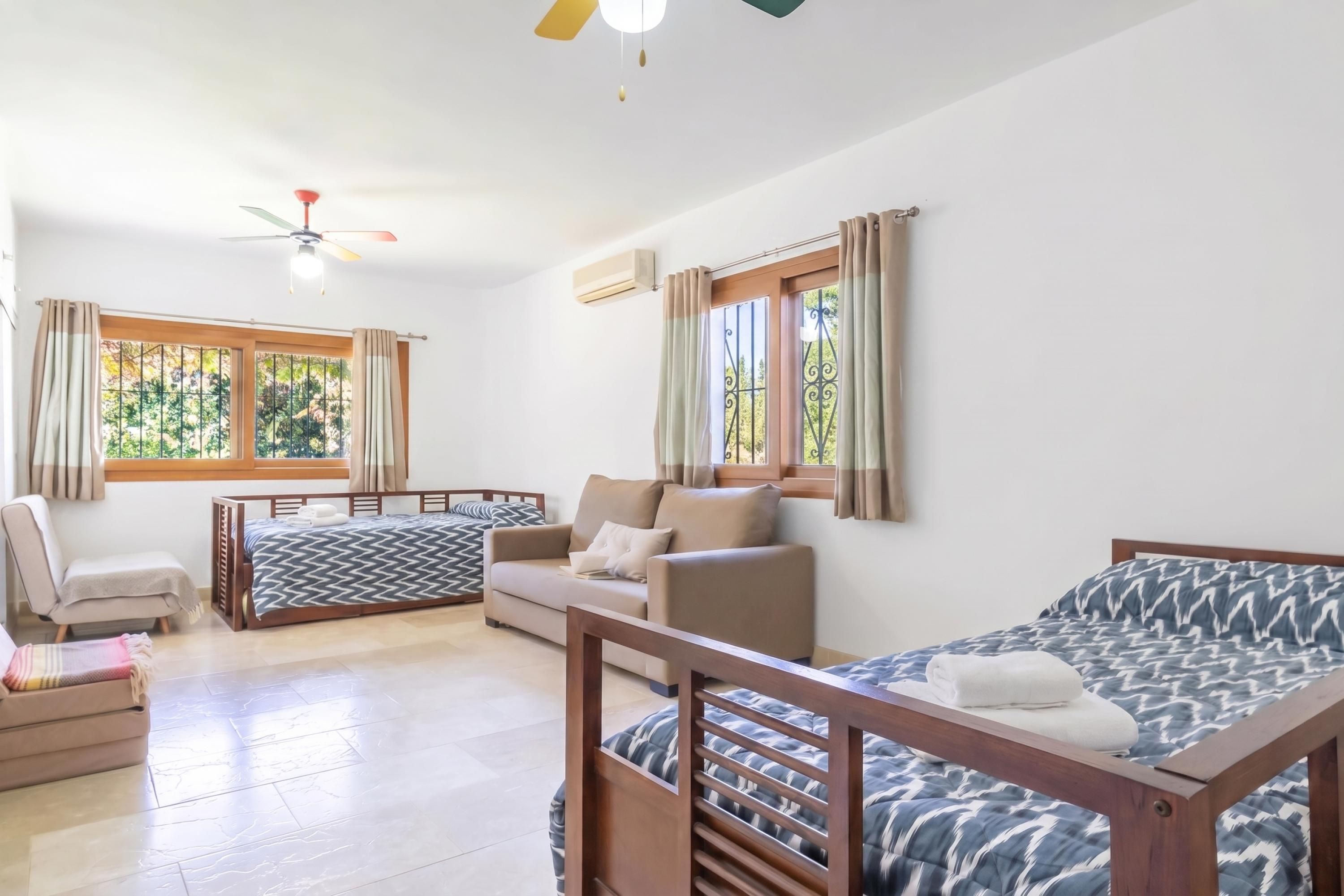 A room with a bed, a sofa, a chair, and a window with curtains.