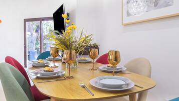 A dining table set with plates, cutlery, and wine glasses, surrounded by colorful chairs.