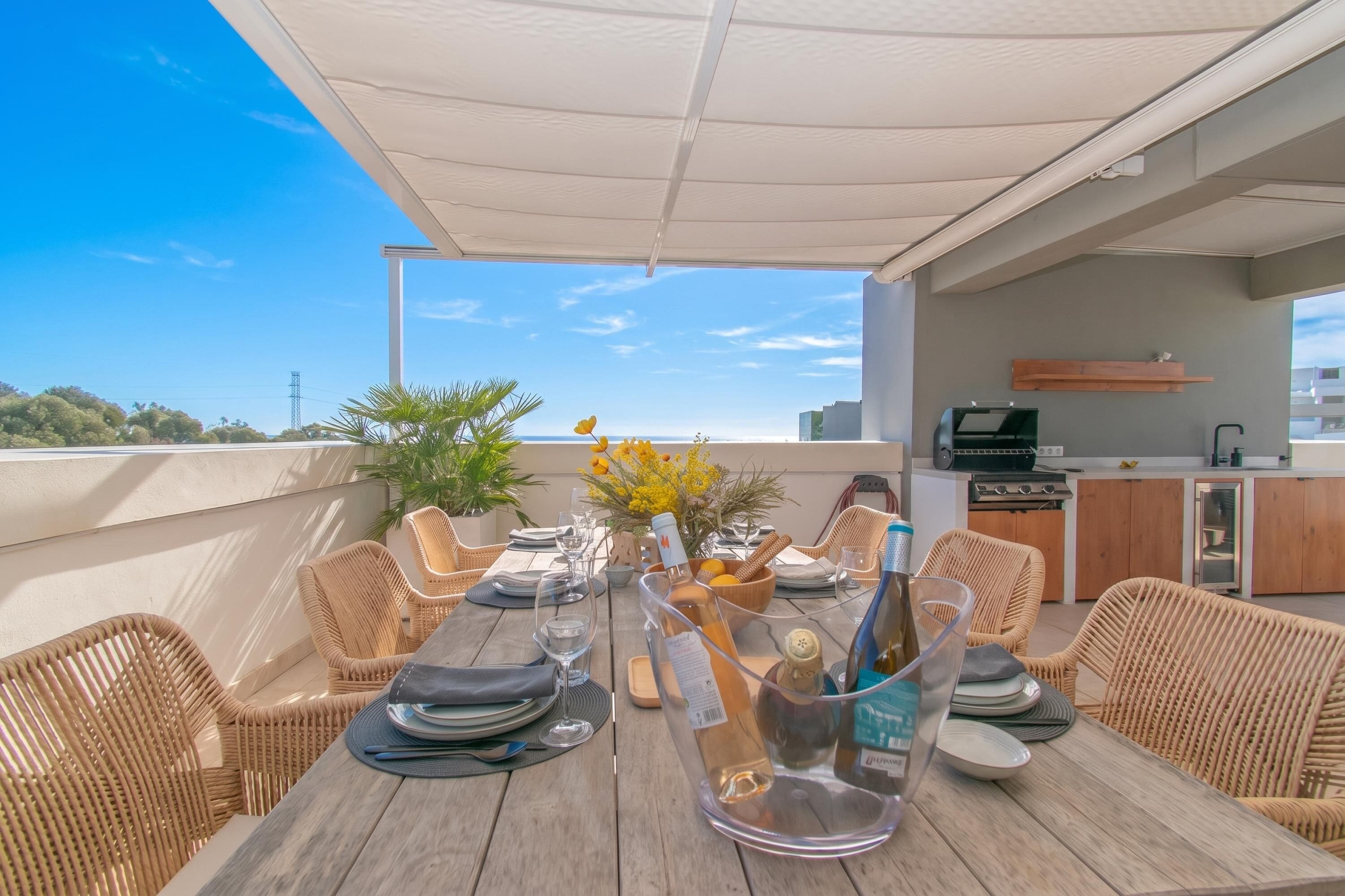 A dining table set for six with wicker chairs, a canopy overhead, and a view of the cityscape.