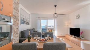 A modern living room with a dining area, a flat-screen TV, and a view of the city. - Cambural Beach Apartment (Fuengirola)