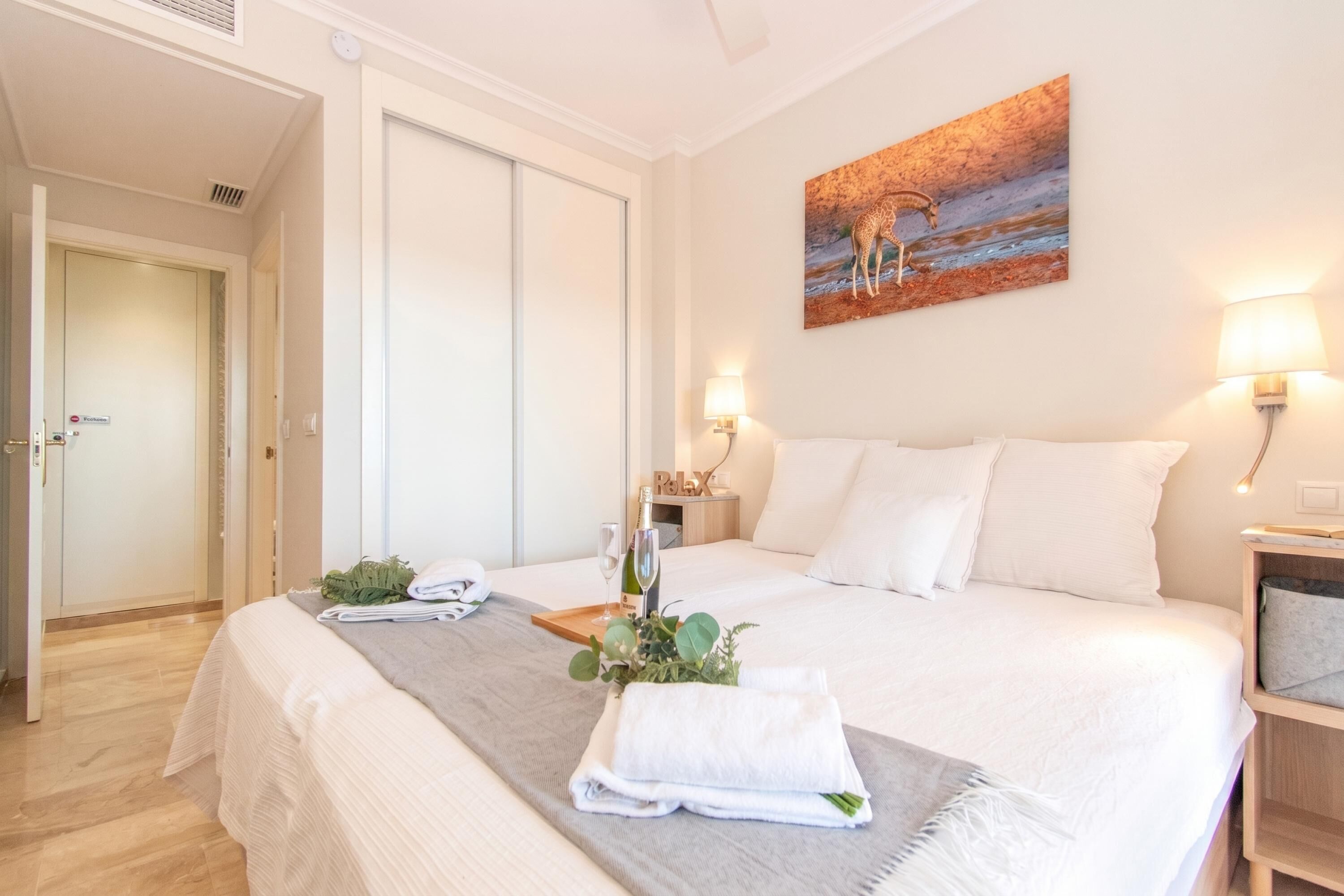 A hotel room with a bed, a painting, a nightstand, and a door.
