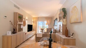 A modern living room with a sofa, a dining table with wine glasses and plates, a TV, and a view of the outdoors. - Paraiso De Riviera (Mijas)