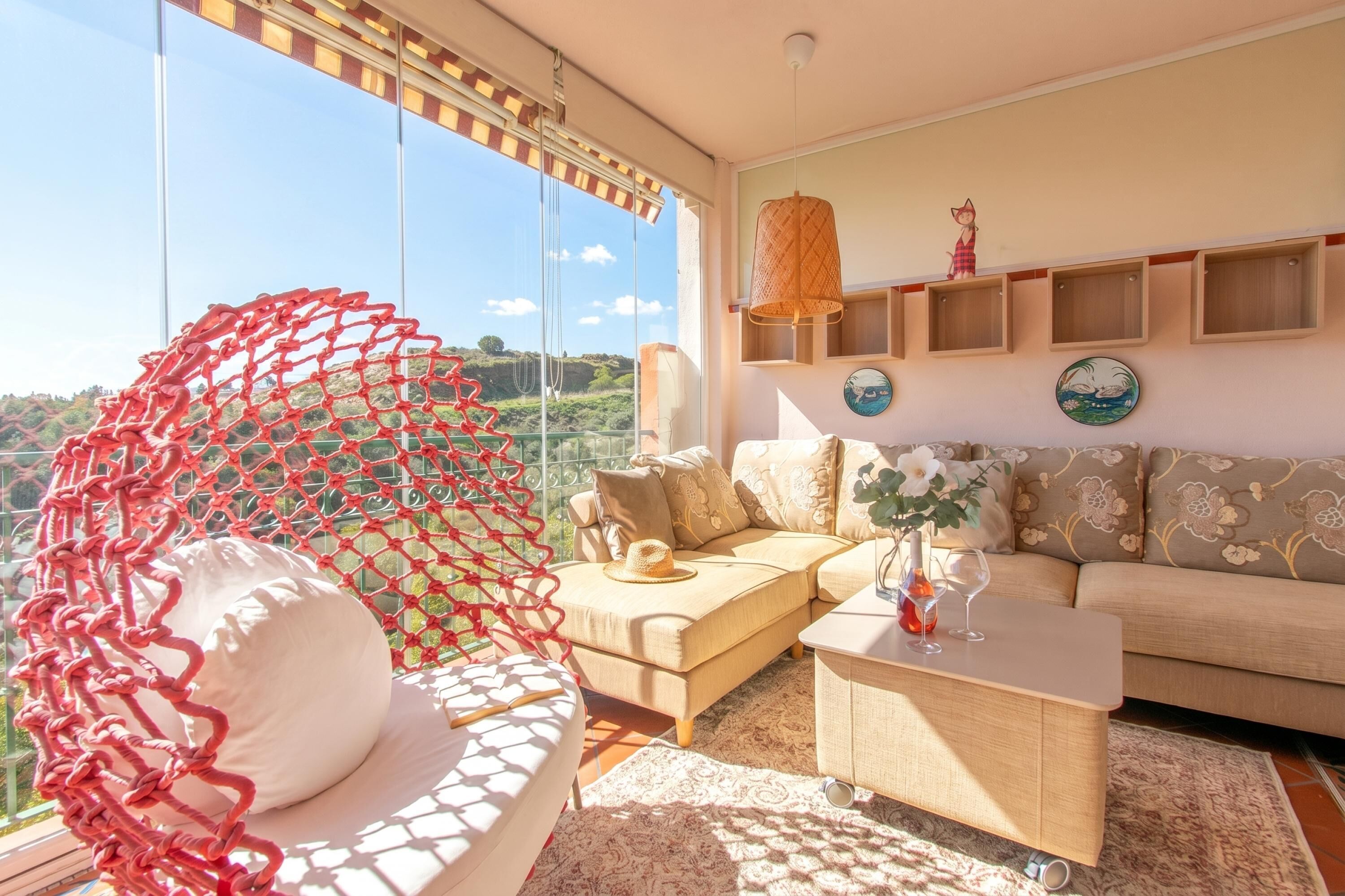 A living room with a sofa, a coffee table, a hanging chair, and a view of the outdoors.