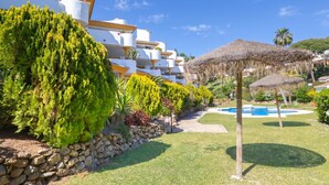A resort with white buildings, a swimming pool, and a thatched umbrella. - Calahonda Golf (Mijas)