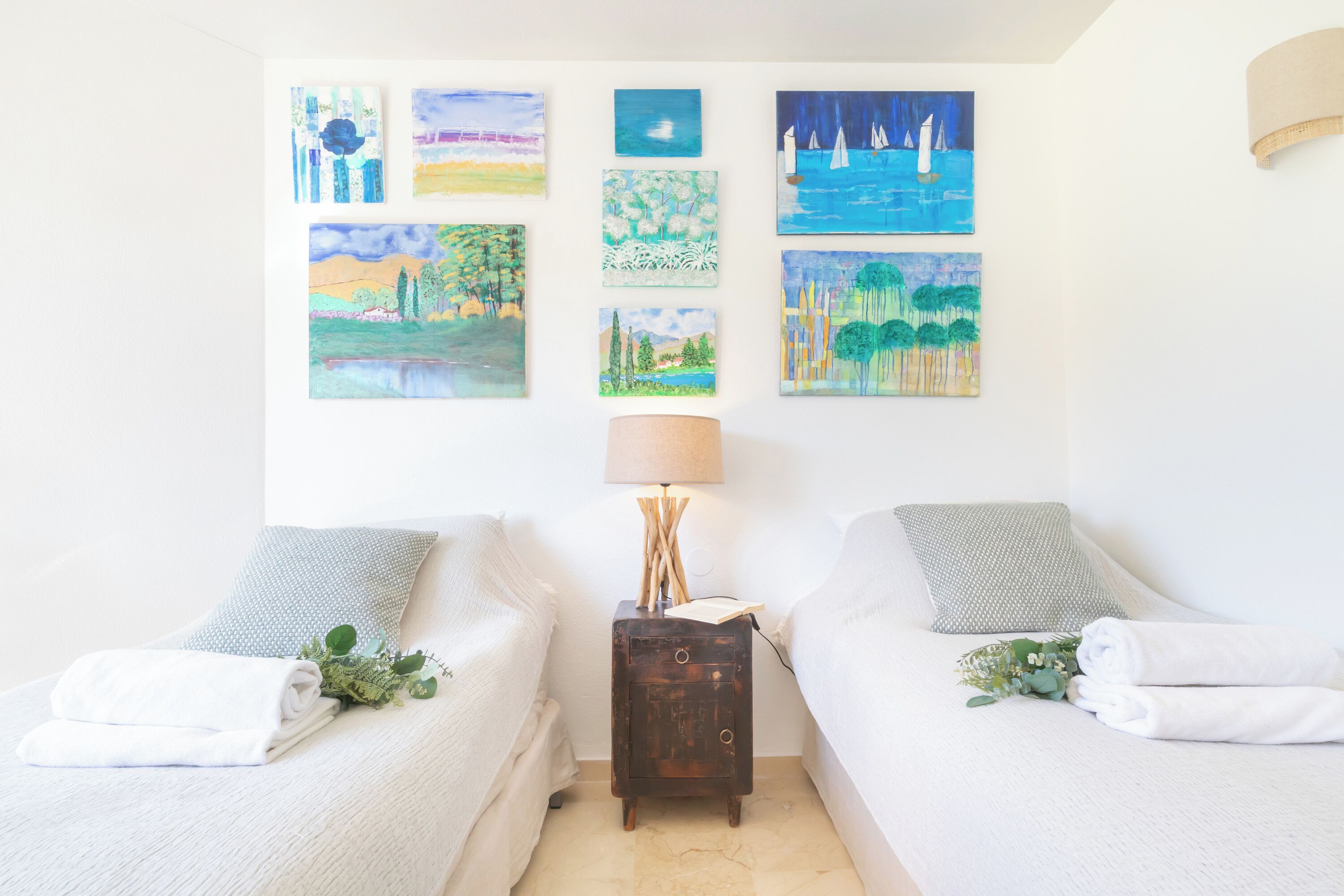 A room with two beds, a nightstand with a lamp, and artwork on the wall.