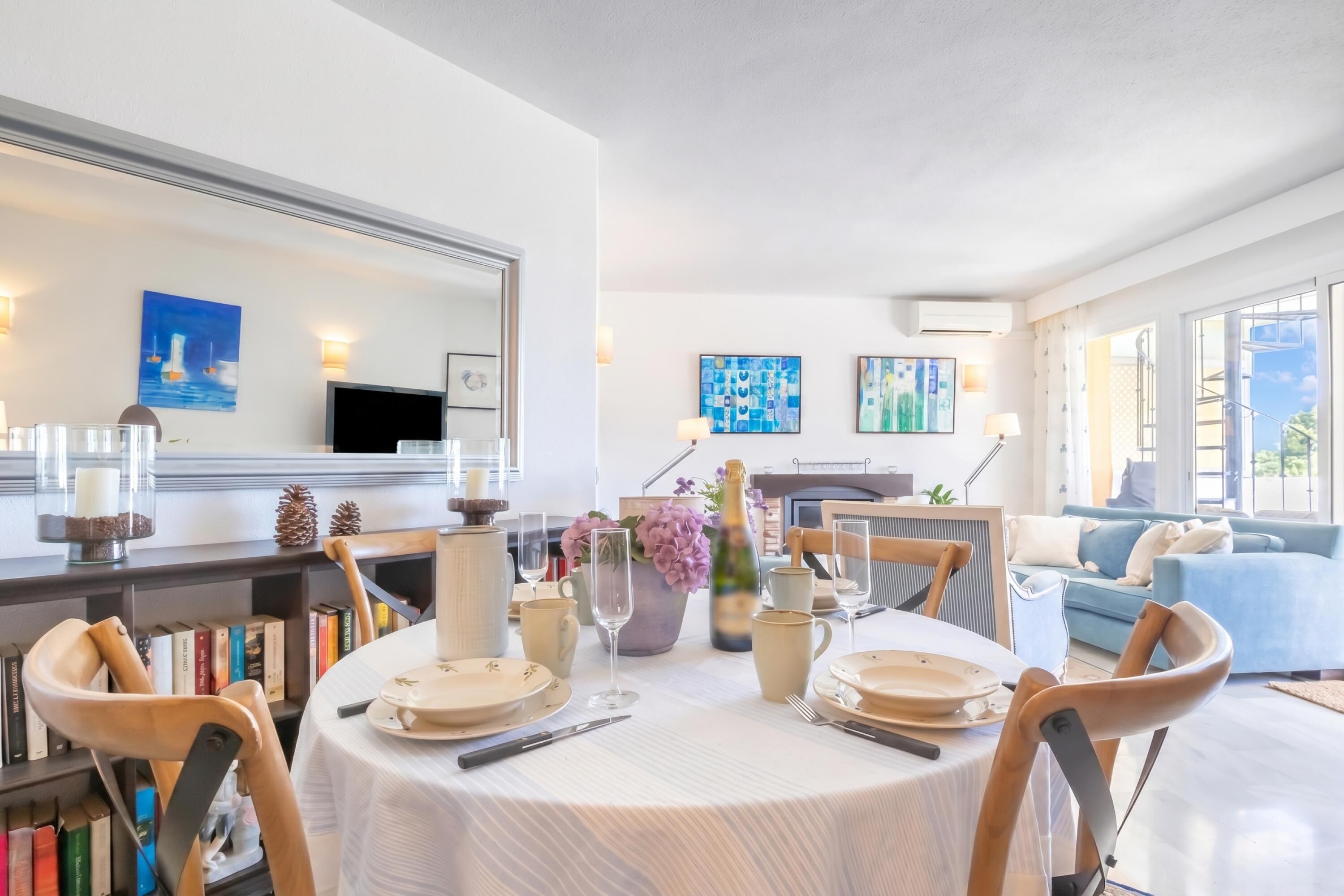 A dining area with a round table set for four, surrounded by bookshelves and a large mirror.