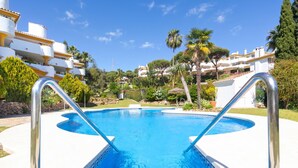 A swimming pool with metal ladders, surrounded by greenery and white buildings. - Calahonda Golf (Mijas)