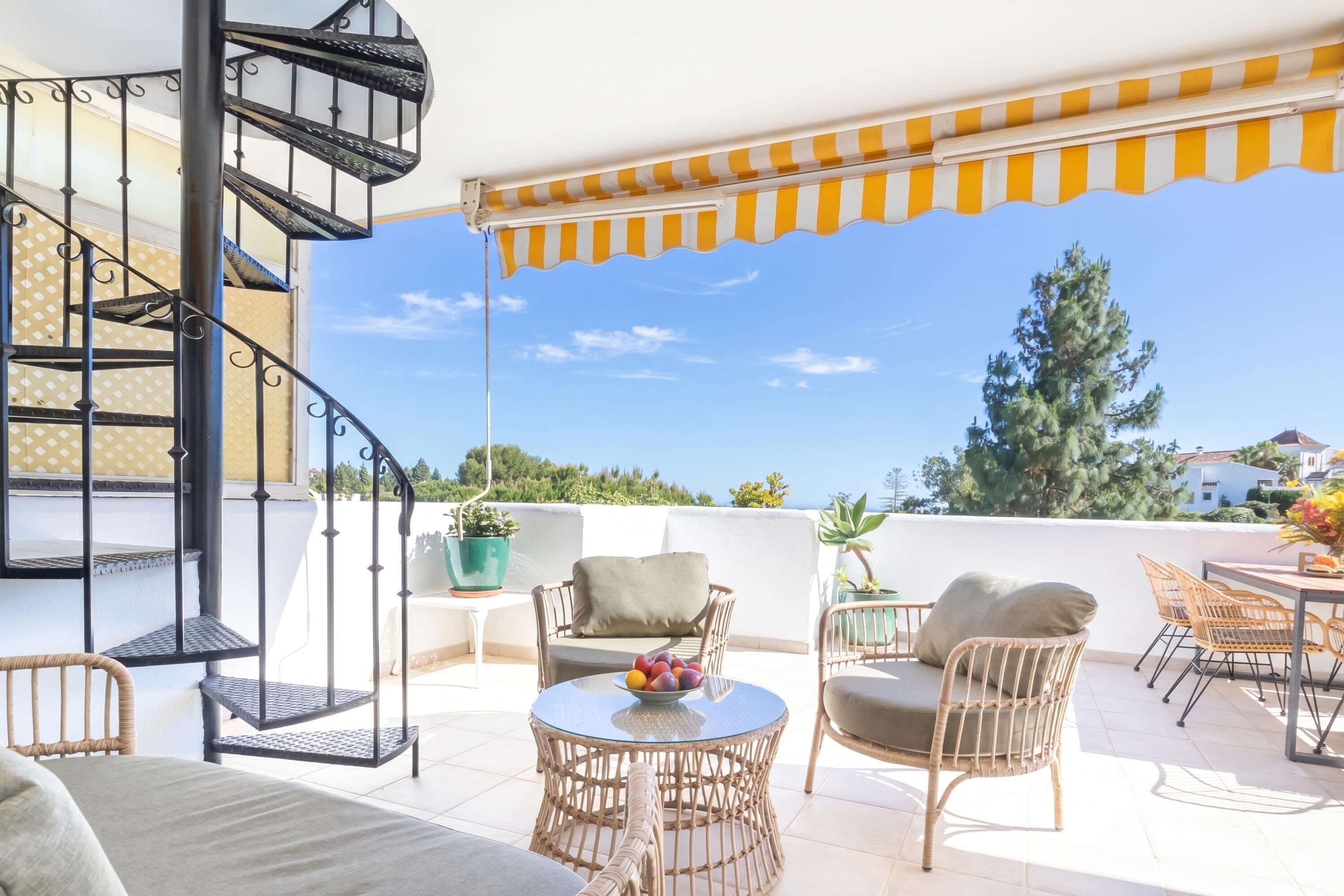 Ein Balkon mit Korbmöbeln, einer Wendeltreppe und Blick aufs Meer.