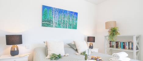 A neatly arranged bedroom with a bed, bedside tables, a bookshelf, and a painting on the wall.