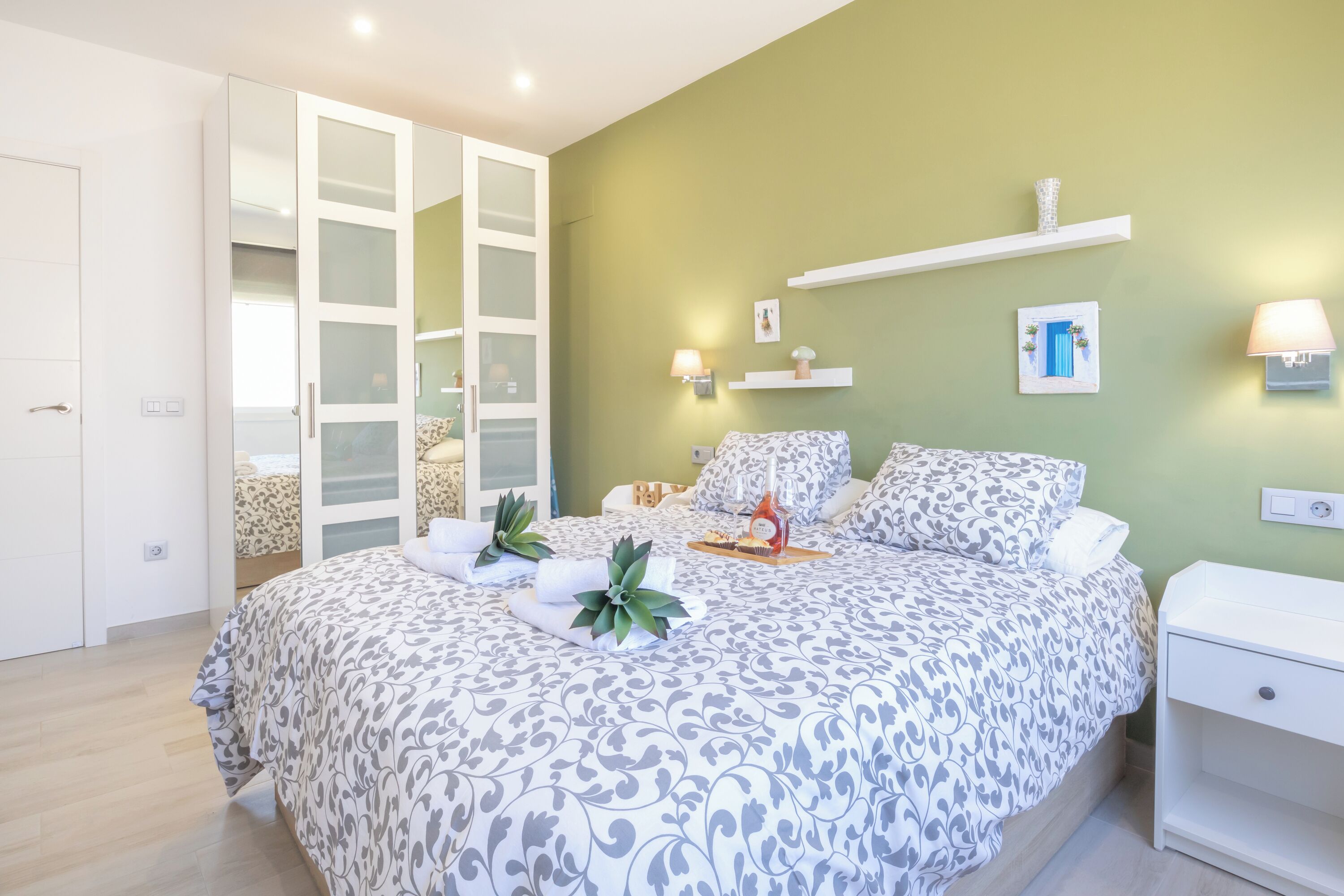 Un dormitorio con cama, mesitas de noche, un armario y una estantería con objetos decorativos.