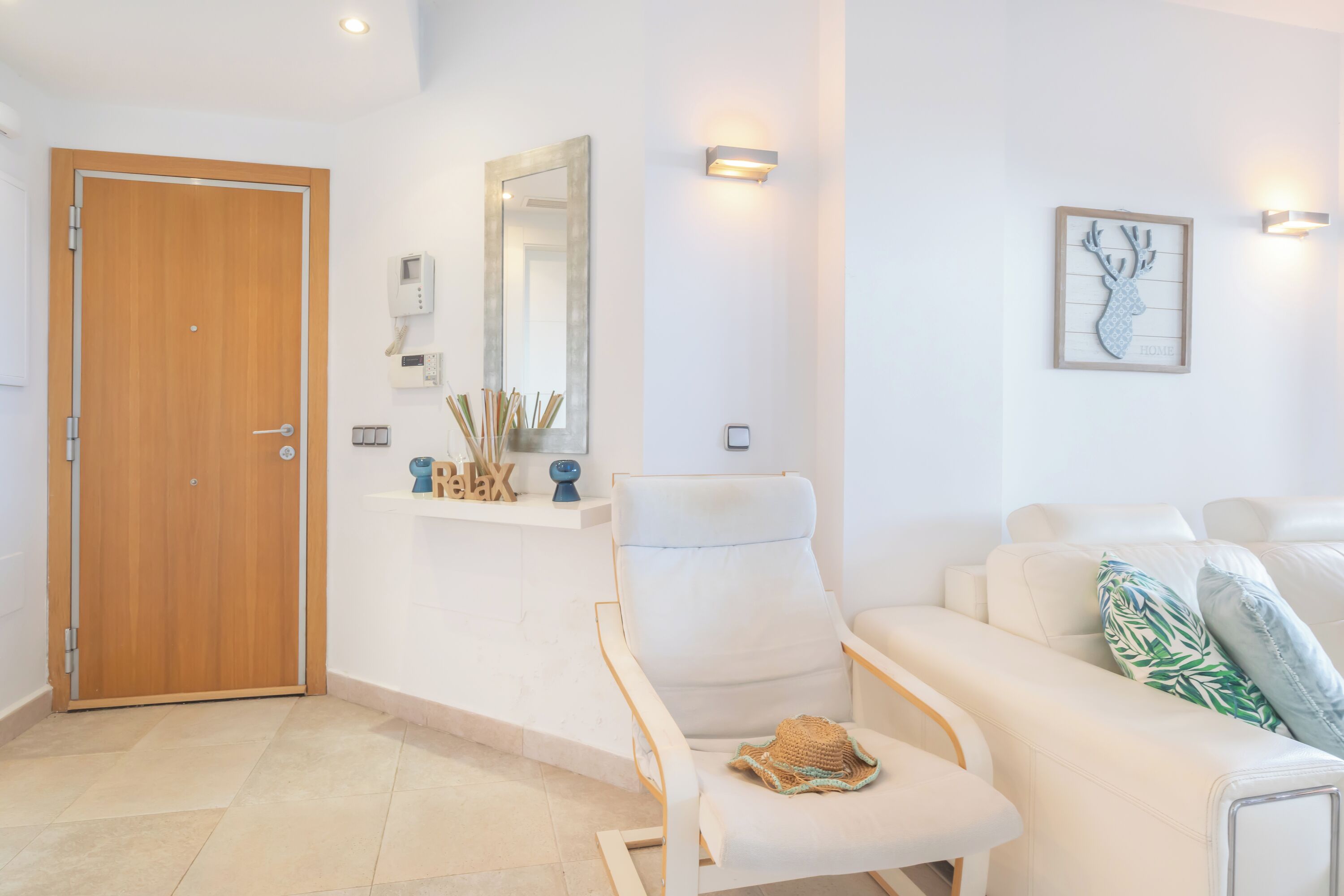 Un salon moderne avec une porte en bois, un fauteuil blanc, un canapé blanc et un miroir fixé au mur.
