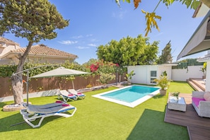 Un patio trasero con piscina, césped artificial, sillas de descanso y una pequeña zona de patio.