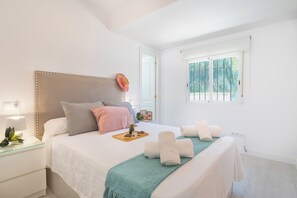 A bedroom with a bed, bedside table, window, and a view of greenery outside. - Villa Caribe Playa (Marbella)