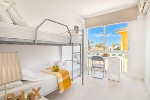 A bunk bed room with a desk and chair, a lamp, and a window with a view of buildings. - Villa Caribe Playa (Marbella)