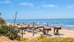 Una playa con sombrillas de paja y sillas de descanso.