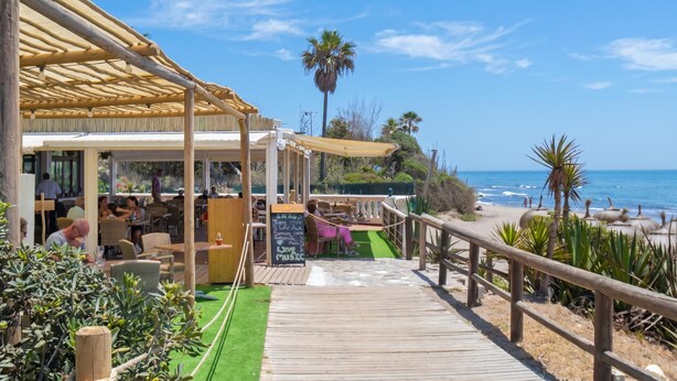 Un restaurante frente a la playa con terraza al aire libre, muelle de madera y vista al océano.