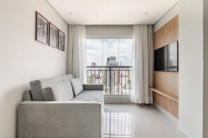 A modern living room with a grey sofa, a mounted TV, and a balcony with a city view. - 360 Paraiso (São Paulo)