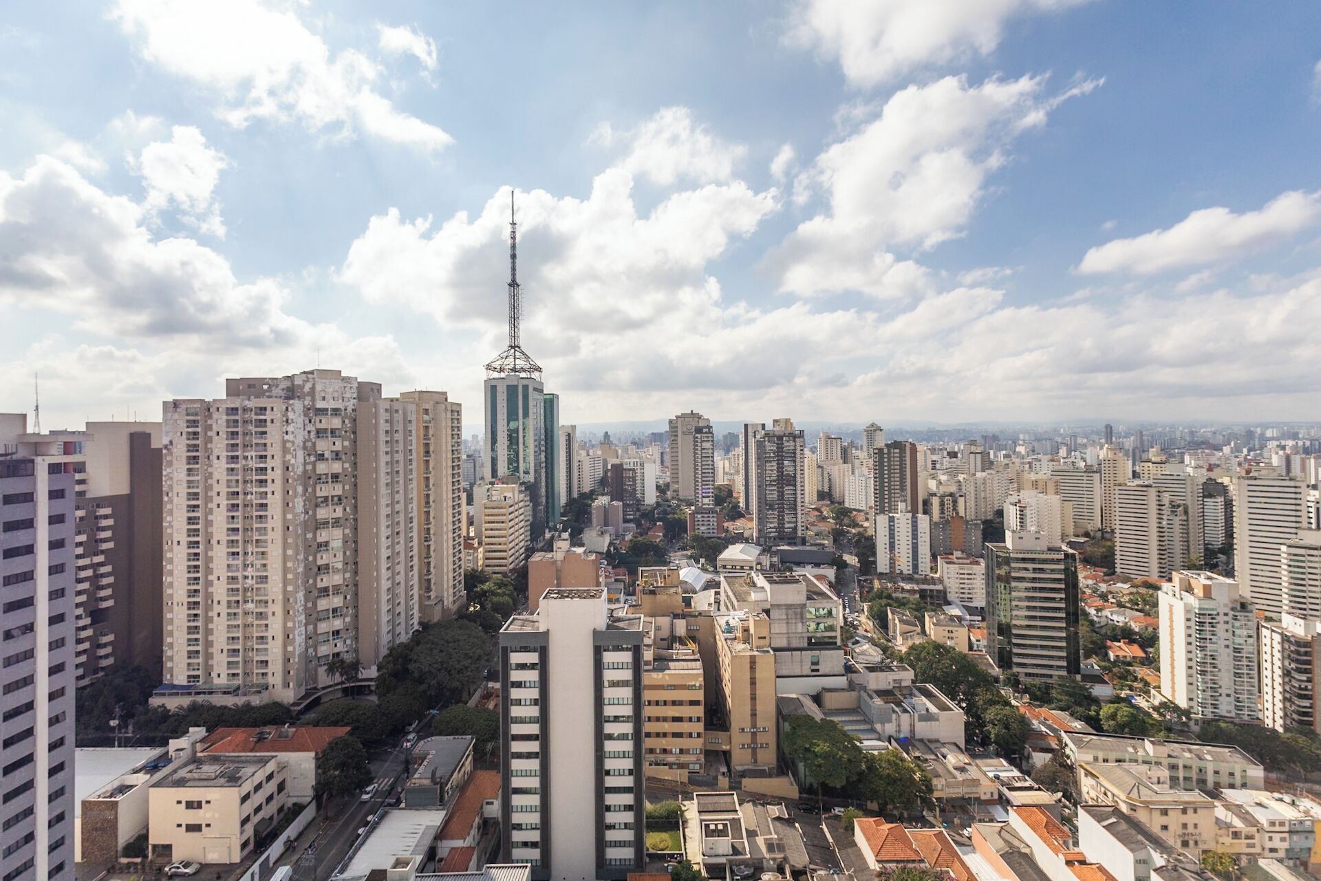 A cityscape with high-rise buildings, including a prominent tower, under a partly cloudy sky.