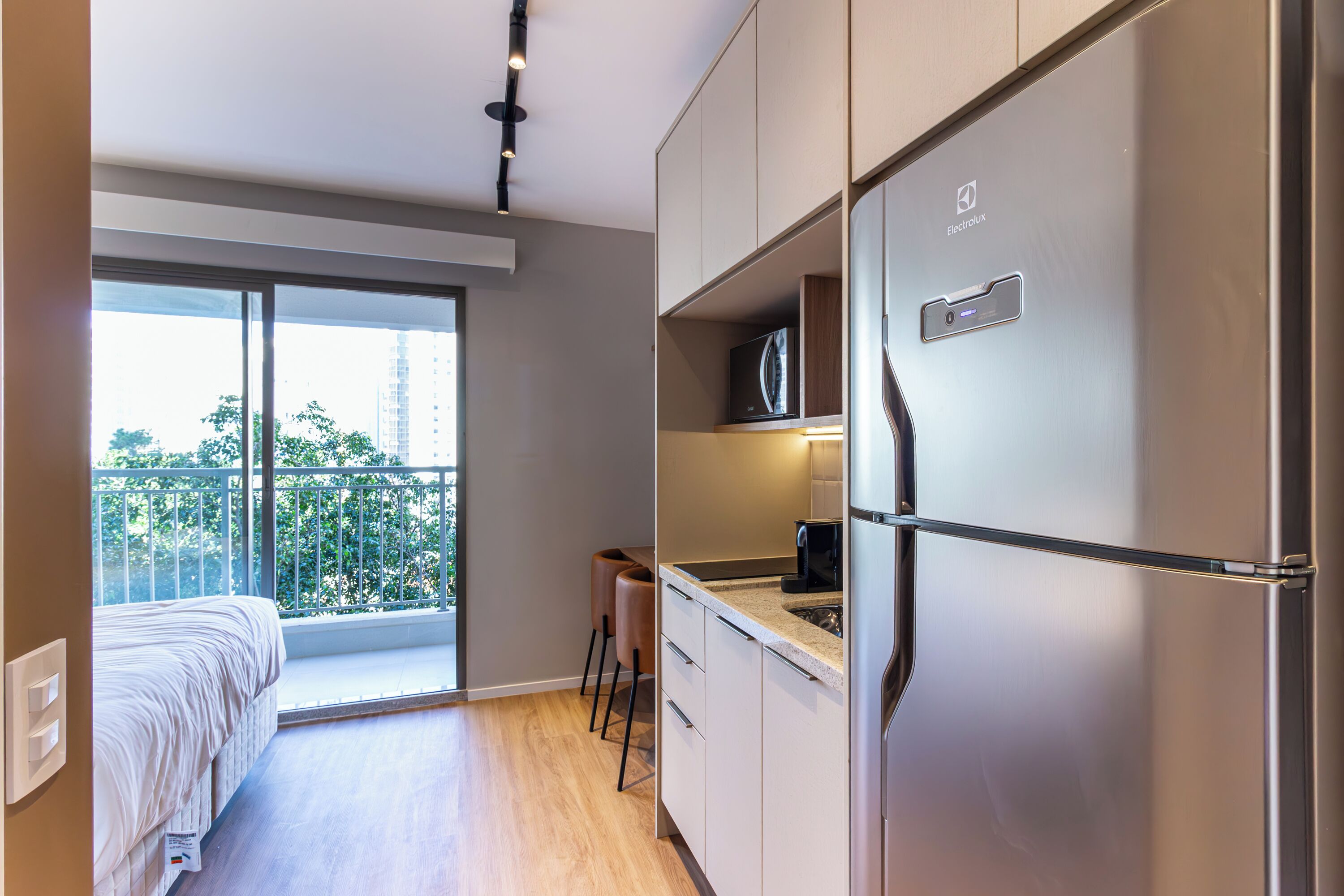 Een moderne keuken met een inbouwkoelkast, een magnetron en een koffiezetapparaat. Er is een balkon met uitzicht op de stad.