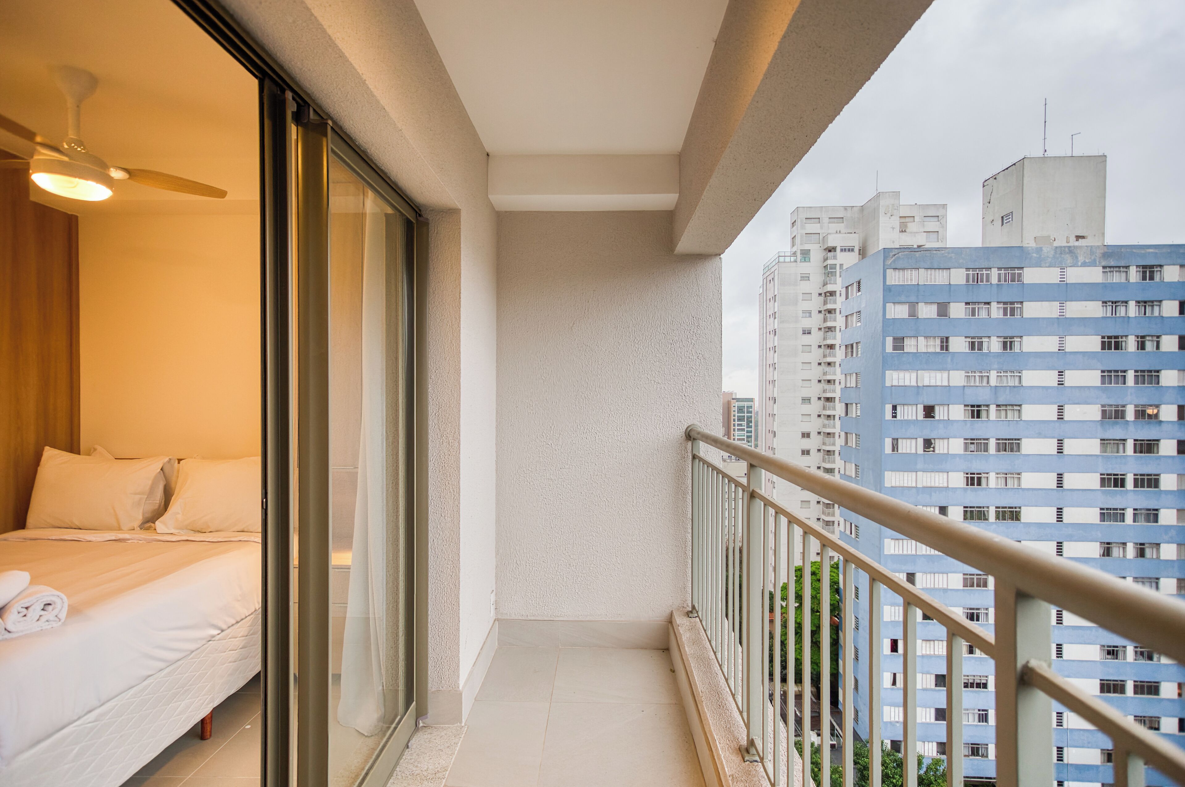 A balcony with a bed, a ceiling fan, and a view of high-rise buildings.