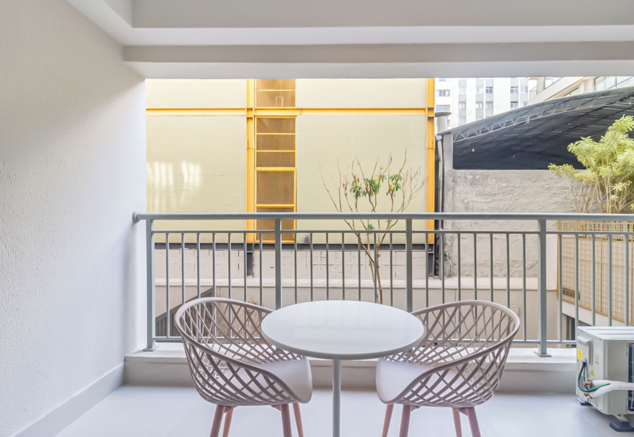 Ein Balkon mit einem weißen Tisch, zwei Korbstühlen, einer gelben Leiter und Blick auf ein Gebäude mit einem schwarzen Dach.