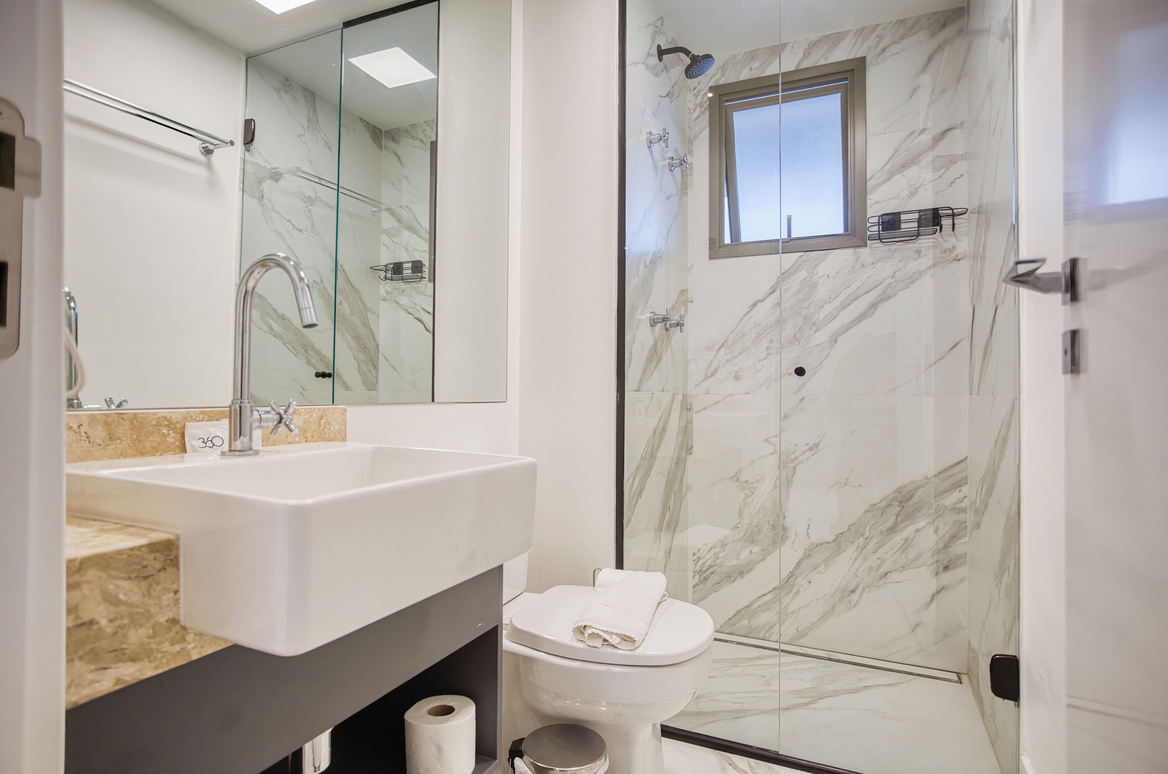 A modern bathroom with a glass-enclosed shower, a white sink, and a marble-tiled shower wall.