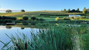 A serene landscape with a calm pond, lush greenery, and a small boat. - 10 ponds, Nature & Architecture, 6-8p (Florennes)