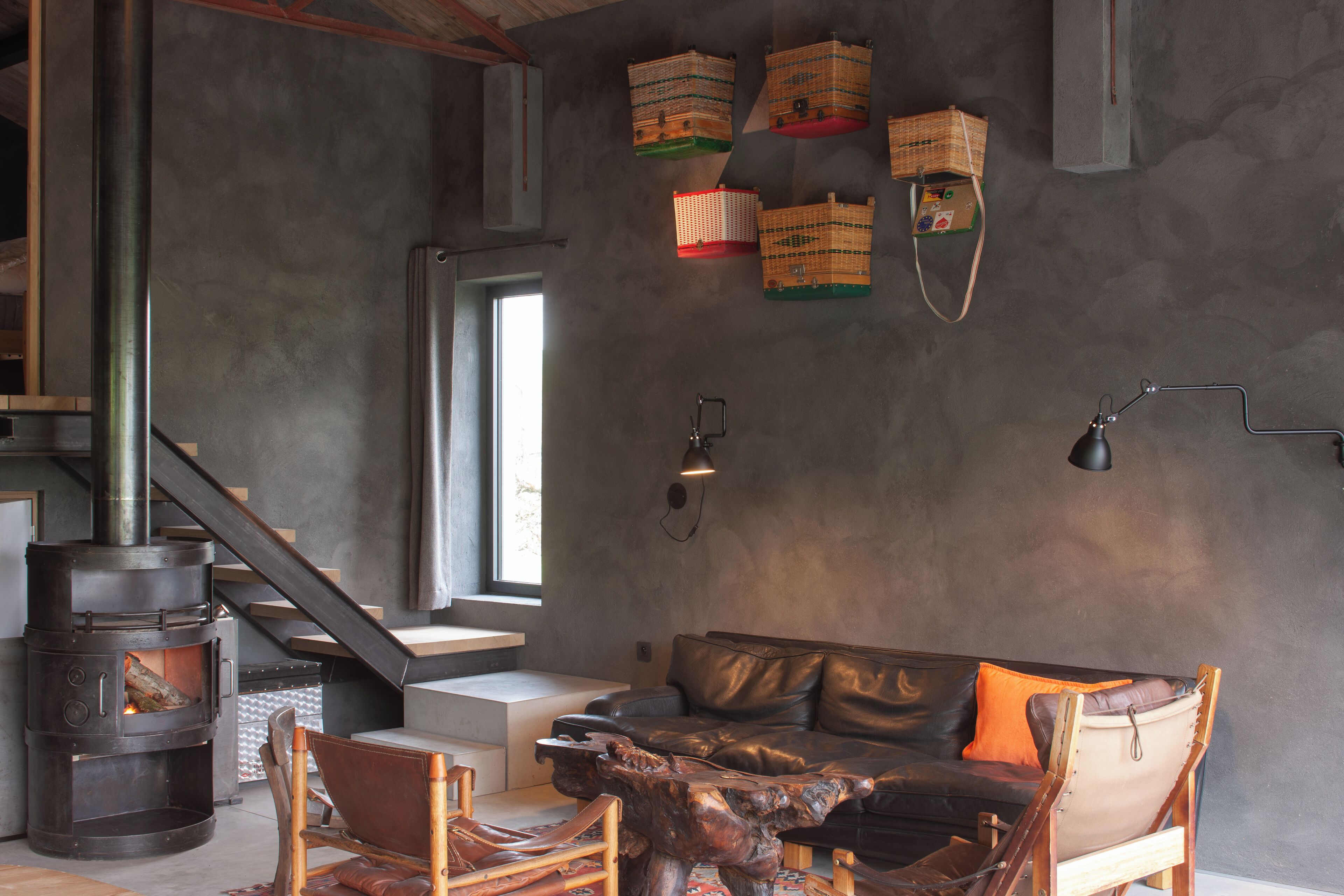 Una sala moderna con chimenea de piedra, sofá de cuero y sillas de madera.