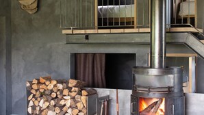 A rustic interior with a wood-burning stove, stacked firewood, a leather chair, and a wooden sculpture. - 10 ponds, Nature & Architecture, 6-8p (Florennes)