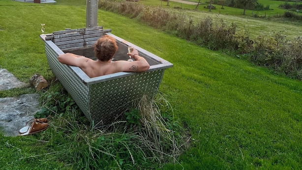 A person relaxing in a metal tub outdoors with a sunset in the background. - 10 ponds, Nature & Architecture, 6-8p (Florennes)