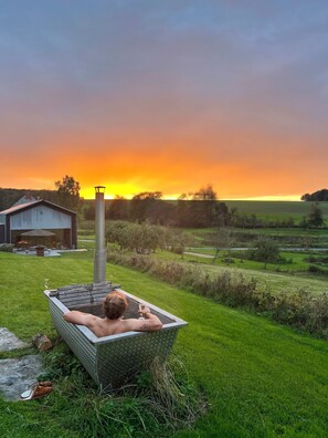 A person relaxing in a metal tub outdoors with a sunset in the background.