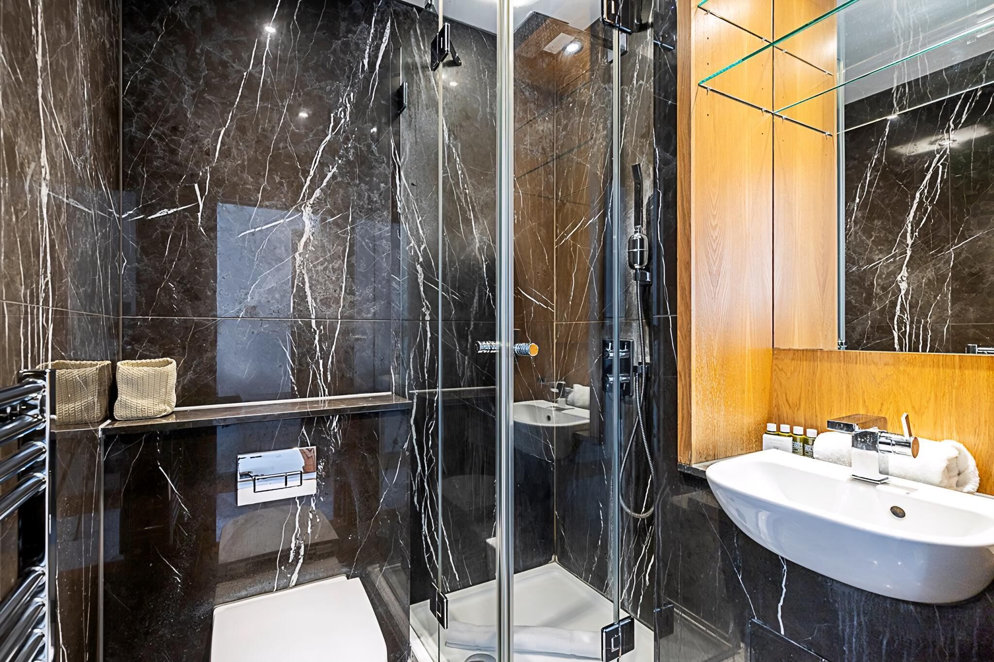 A modern bathroom with a glass-enclosed shower, a white sink, and marble walls.