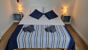 Een net opgemaakt bed met een gestreepte plaid, twee kussens en twee opgerolde handdoeken. Aan beide zijden van het bed staan nachtkastjes met lampen.