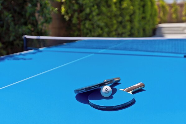 A blue table tennis table with a net, two paddles, and a ball. - LAZY RIVER• Splash park• Pedal boats• Water slide• Theater• Arcades• Volleyball (Coachella)