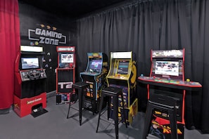 A gaming zone with arcade machines, stools, and a curtain backdrop. - LAZY RIVER• Splash park• Pedal boats• Water slide• Theater• Arcades• Volleyball  (Coachella)