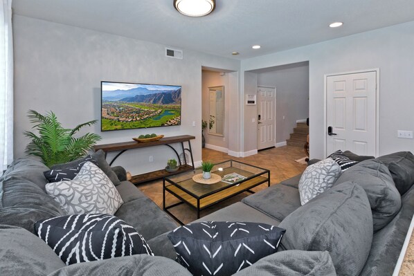 A modern living room with a gray sectional sofa, a glass coffee table, and a large landscape painting on the wall. - LAZY RIVER• Splash park• Pedal boats• Water slide• Theater• Arcades• Volleyball  (Coachella)