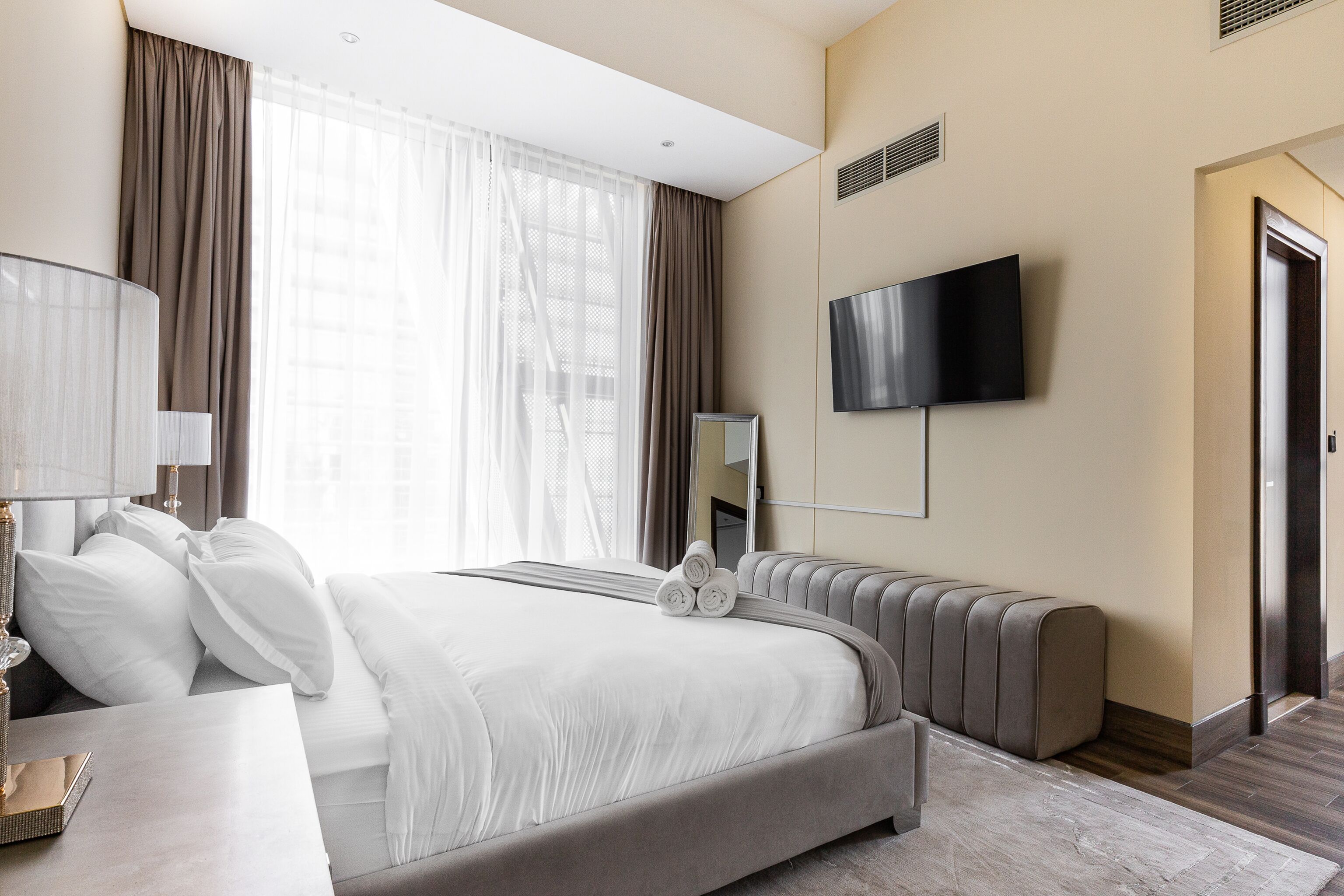 Habitación de hotel moderna con una cama grande, televisor de pantalla plana, mesita de noche y un ventanal con cortinas.