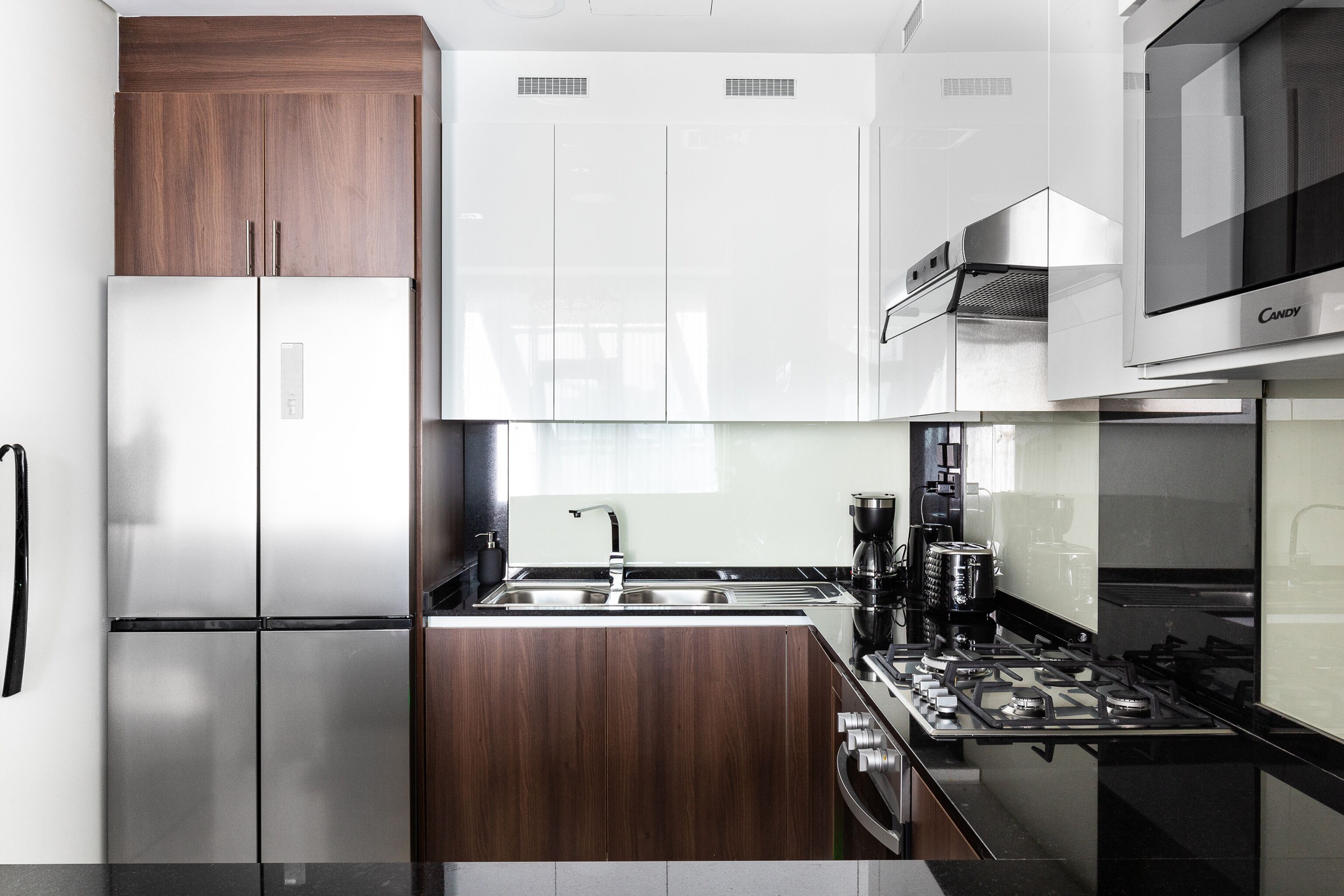 A modern kitchen with a stainless steel refrigerator, wooden cabinets, a black countertop, and a gas stove.