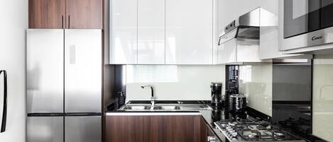 A modern kitchen with a stainless steel refrigerator, wooden cabinets, a black countertop, and a gas stove.