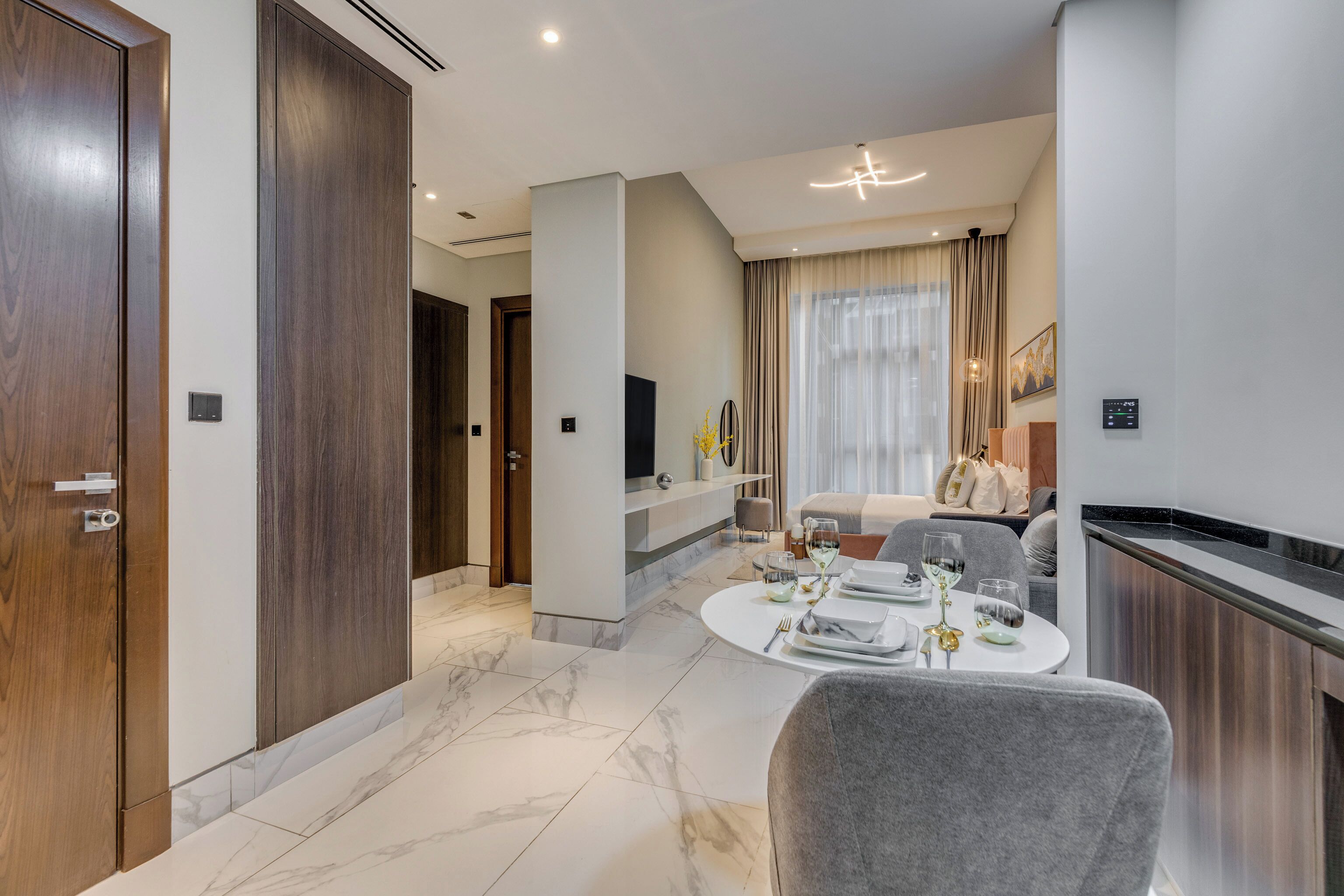 Una sala de estar moderna con comedor, que presenta suelo de mármol, puertas de madera y un televisor montado en la pared.