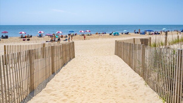 Una playa arenosa con una cerca de madera en el centro, que lleva al océano.