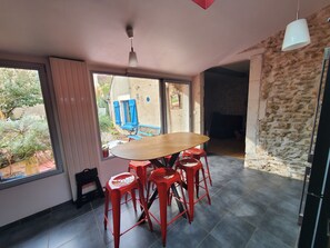 Ein Essbereich mit einem Holztisch und roten Hocker, großen Fenstern mit Blick auf Grünflächen und einer Steinwand.