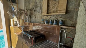 A kitchen with a stone backsplash, a gas stove, a sink, and a shelf with cleaning supplies. - Classic 3-bedrooms apartment with swimming pool in Meronas (Meronas)