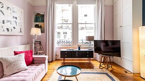 A living room with a pink sofa, a coffee table, a TV, and a window with curtains. - Lovely One-bedroom Flat Near West Kensington (London)