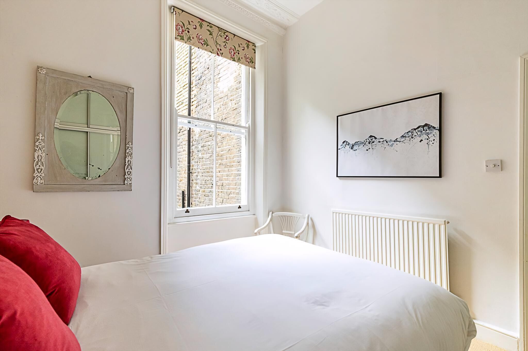 A bedroom with a large bed, a window with a view of a brick building, a radiator, and a framed artwork on the wall.