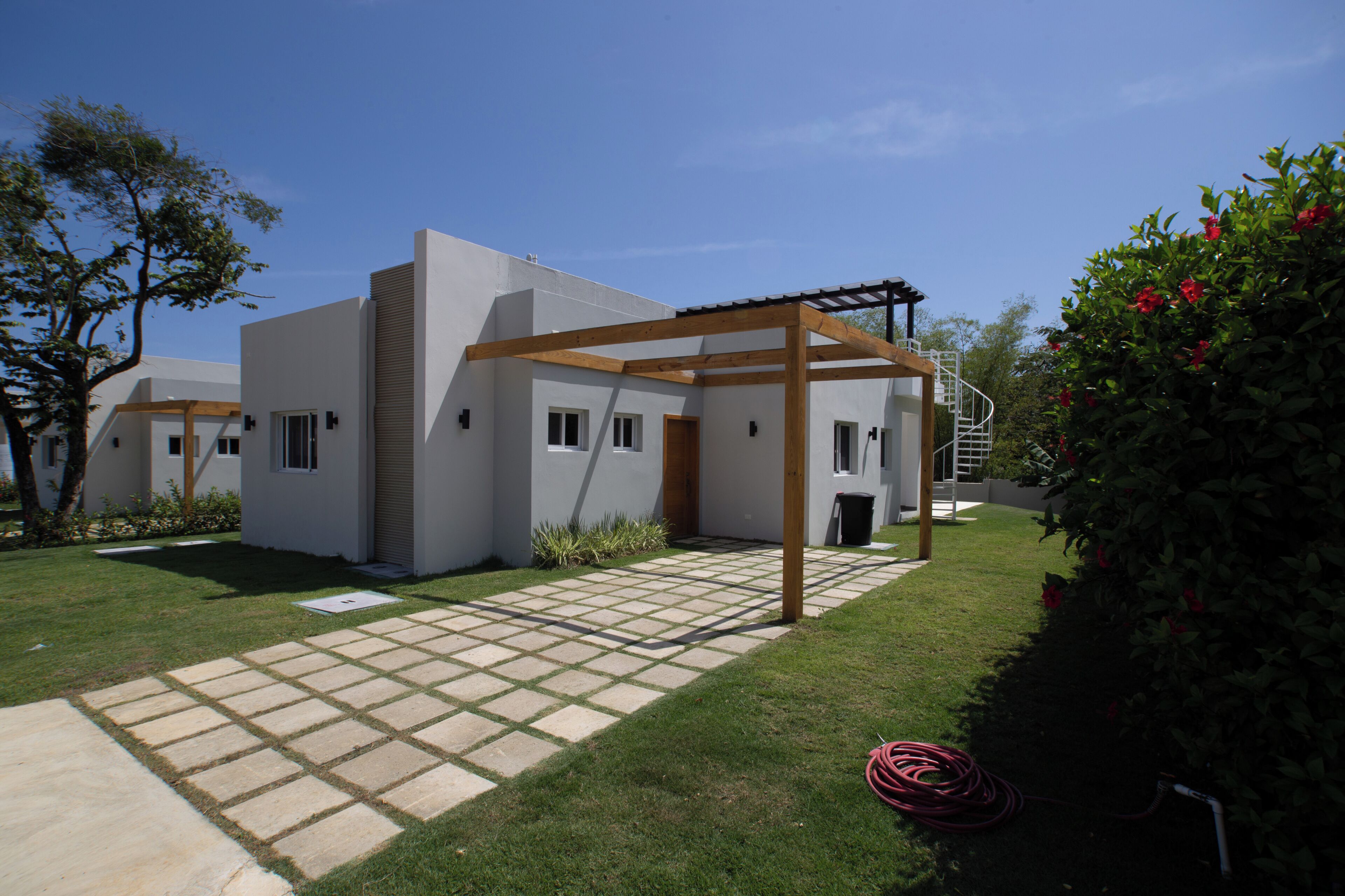 A modern house with a covered patio, a paved walkway, and a garden with a hose.